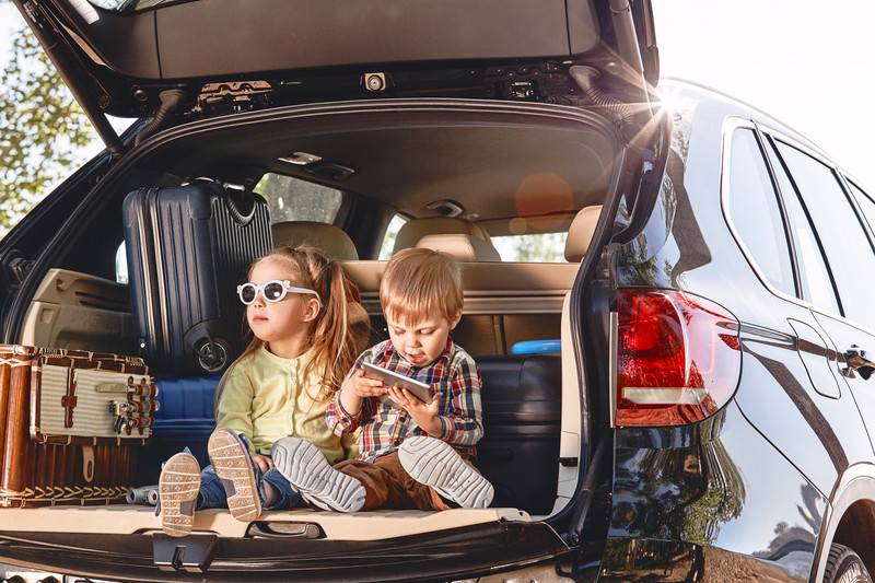 Kids sitting in the trunk of car while its being packed for road trip